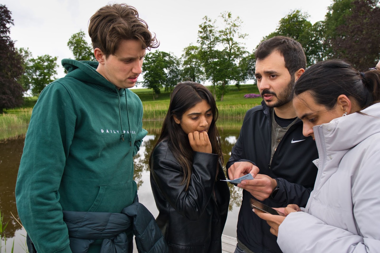 Photo of four Leapsome employees standing by the lake solving a clue for the treasure hunt