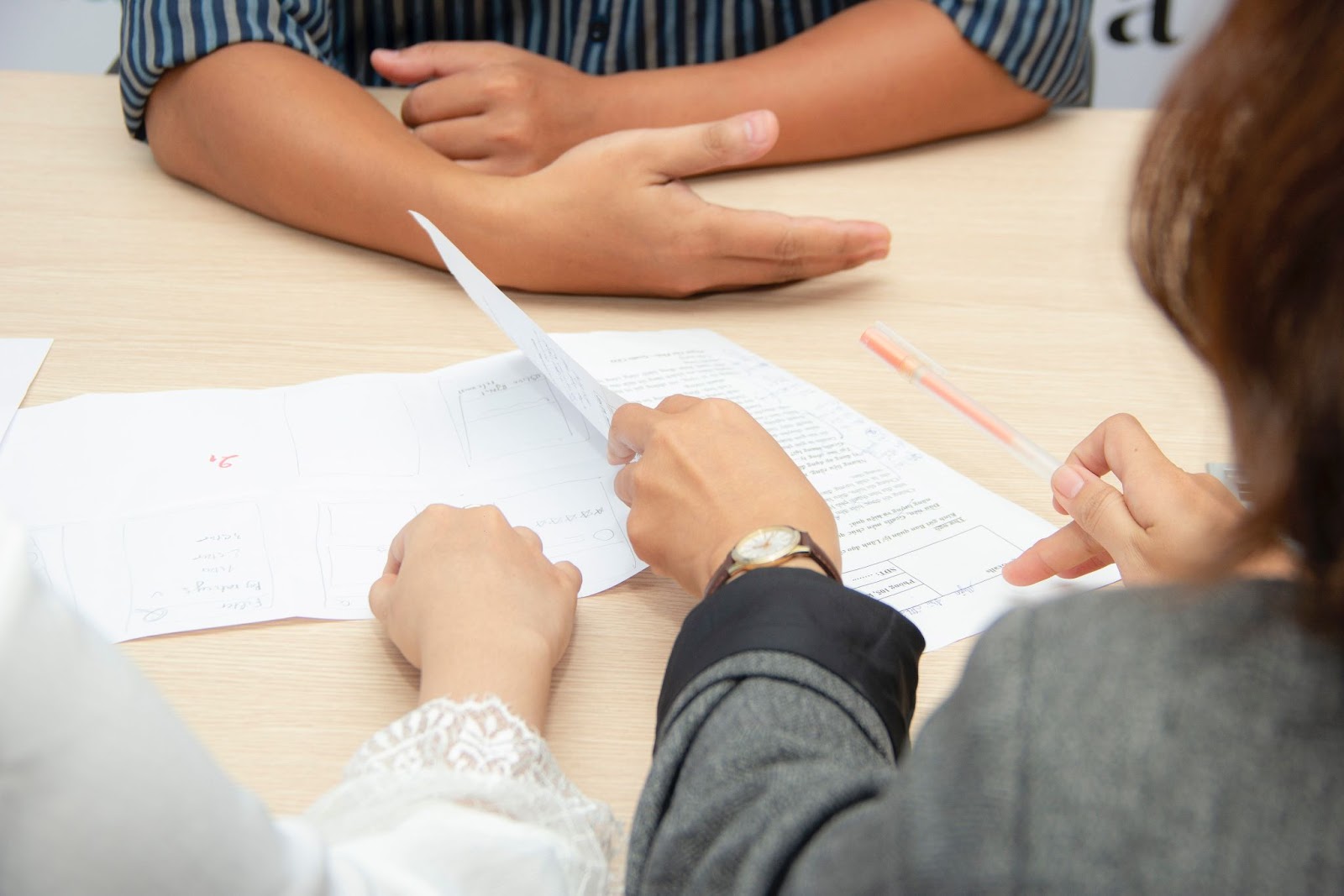 The hands and arms of three employees are shown, and they are sitting at a table with papers on it, seemingly in an interview.