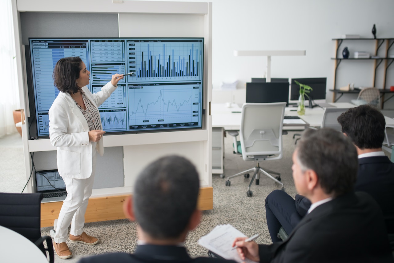 Photo of a woman giving a presentation to employees, and on the board you can see graphic organizers with data