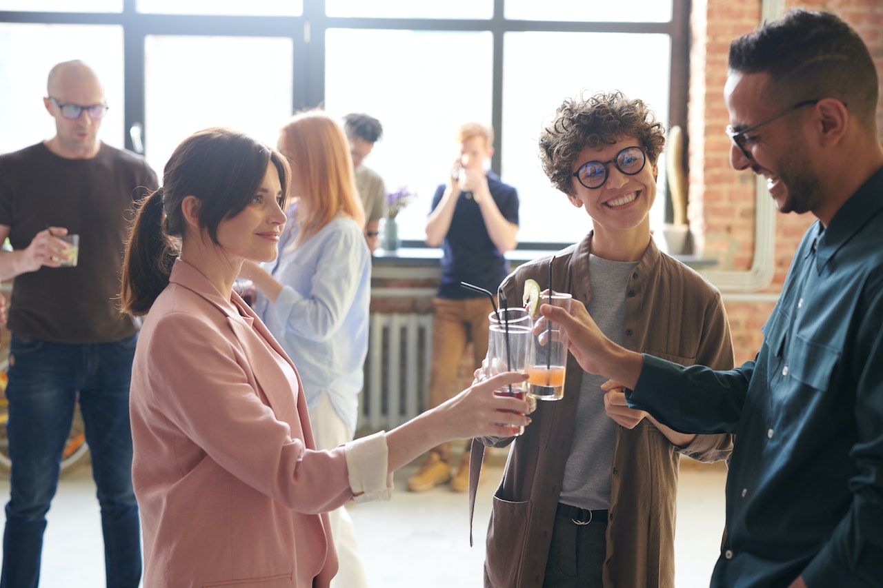 Photo of employees at a work event, three of them bringing their drink glasses together in celebration