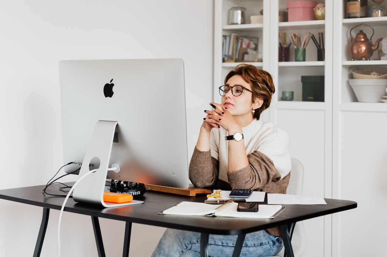 Photo of an employee at her home desk, thinking in front of her computer