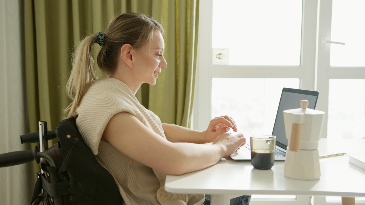 A photo of a person sitting behind a table working on their laptop.