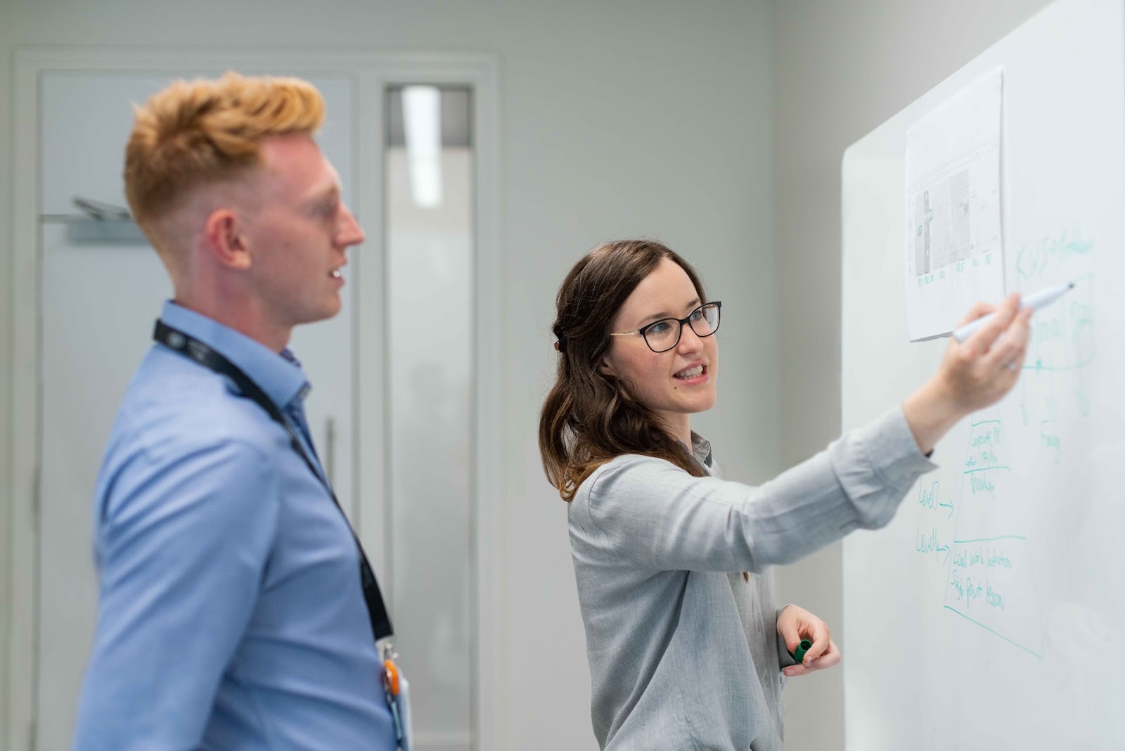 Photo of one employee presenting something on a white board to another employee