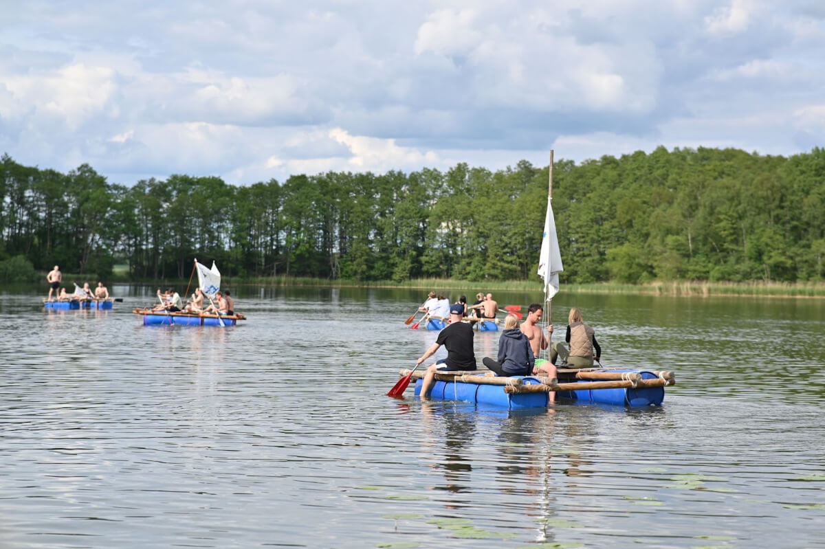 Photo of two Leapsome employees testing the raft they built by sitting on barrels in a lake.