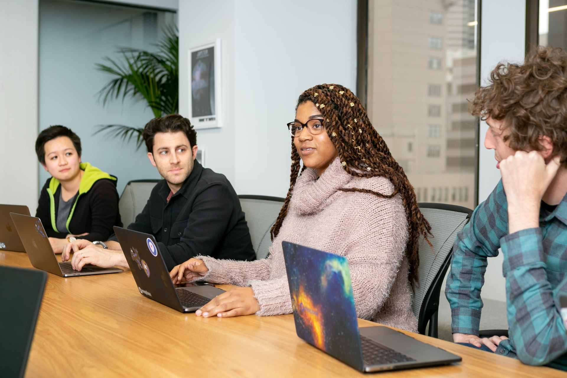 A photo of four employees sitting at a table having a meeting, each with laptops in front of them