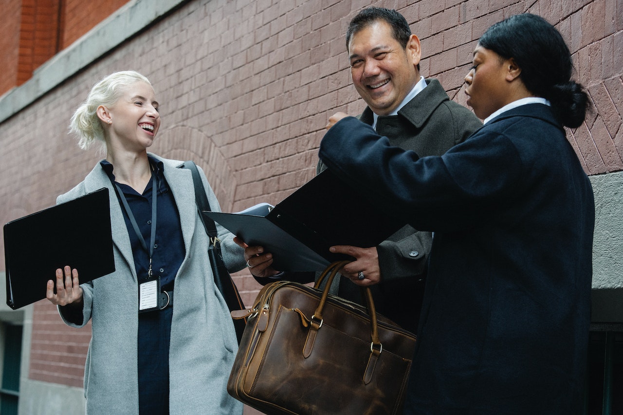 Photo of three professionals standing outside a building, holding folders and looking happy