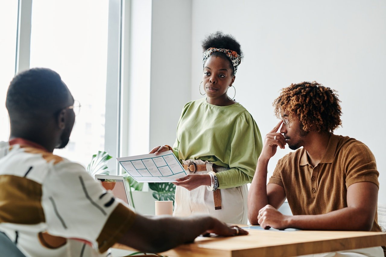 A photo of a manager presenting to two colleagues in a meeting room.