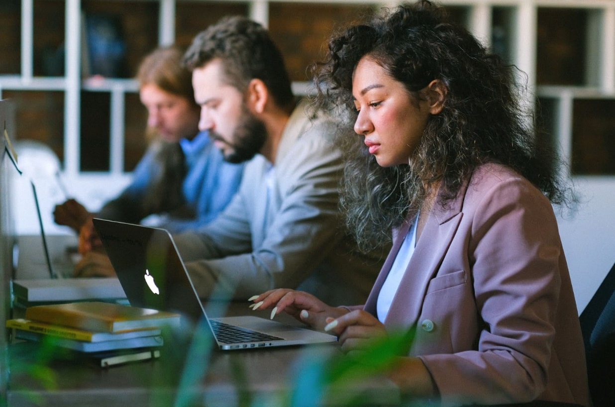 A photo of employees working at laptop computers at their desks.