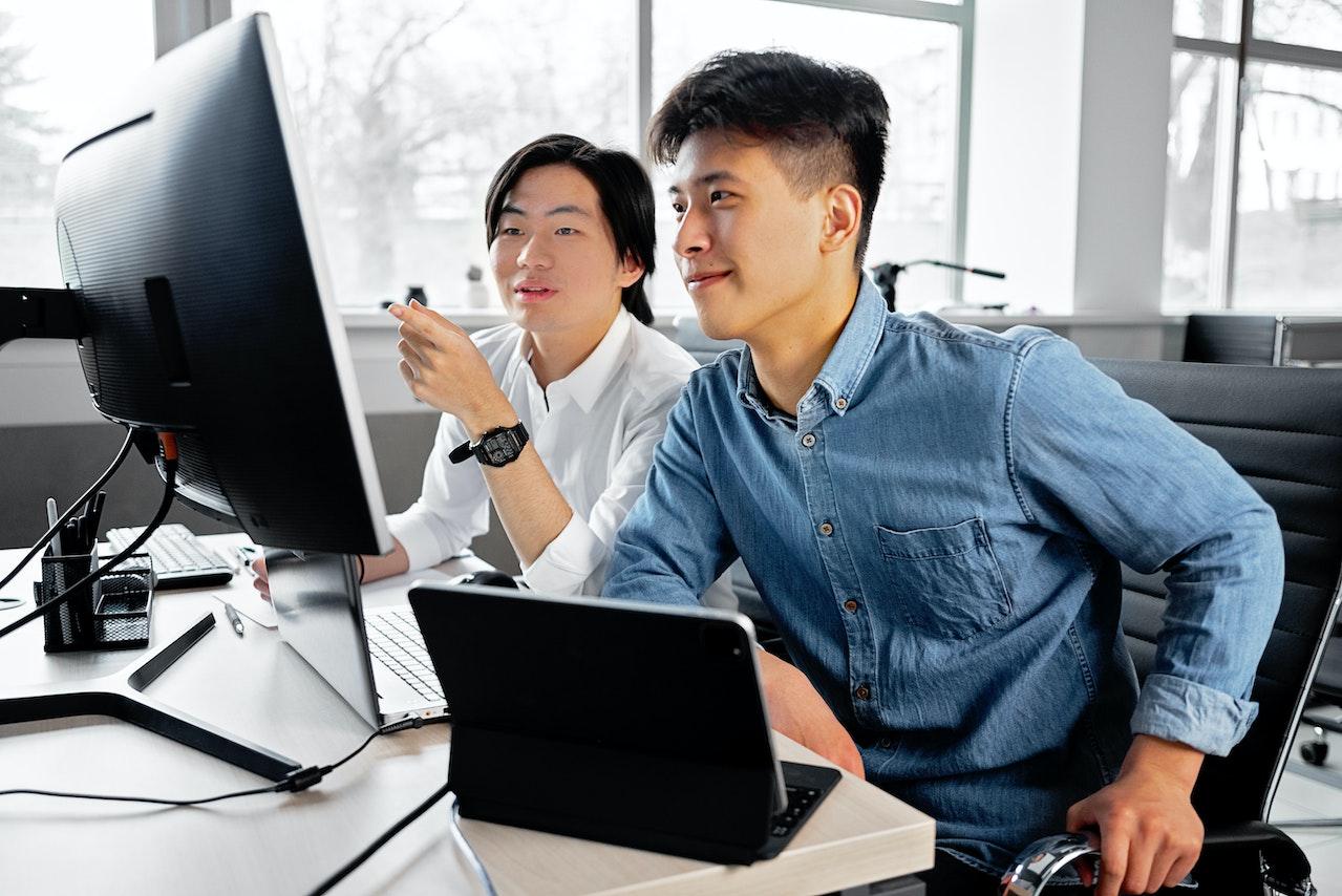 A photo of two of employees working together at a desk, one mentoring the other.