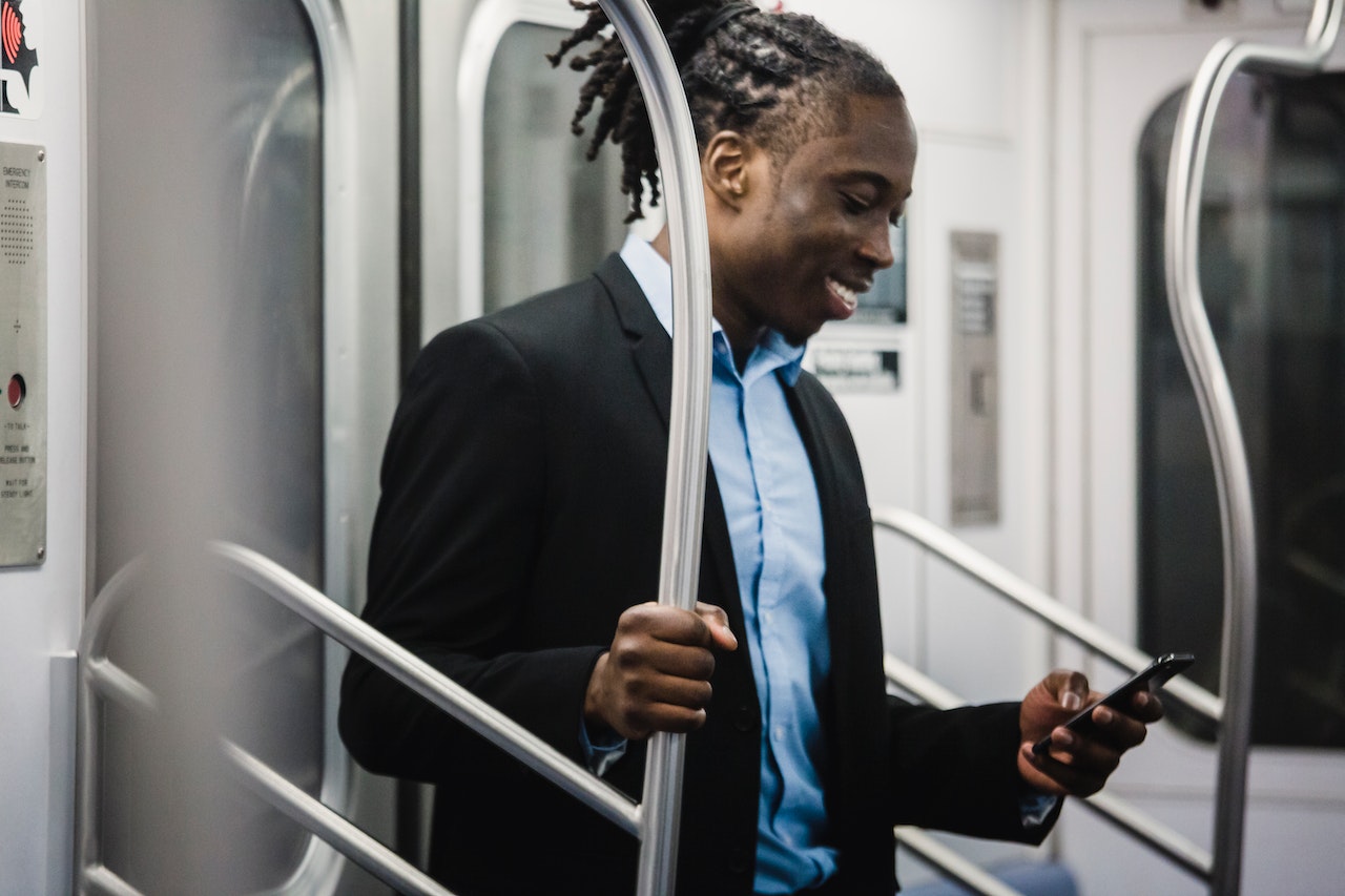 Photo of a man standing on an empty subway train and smiling as he reads a smartphone screen.