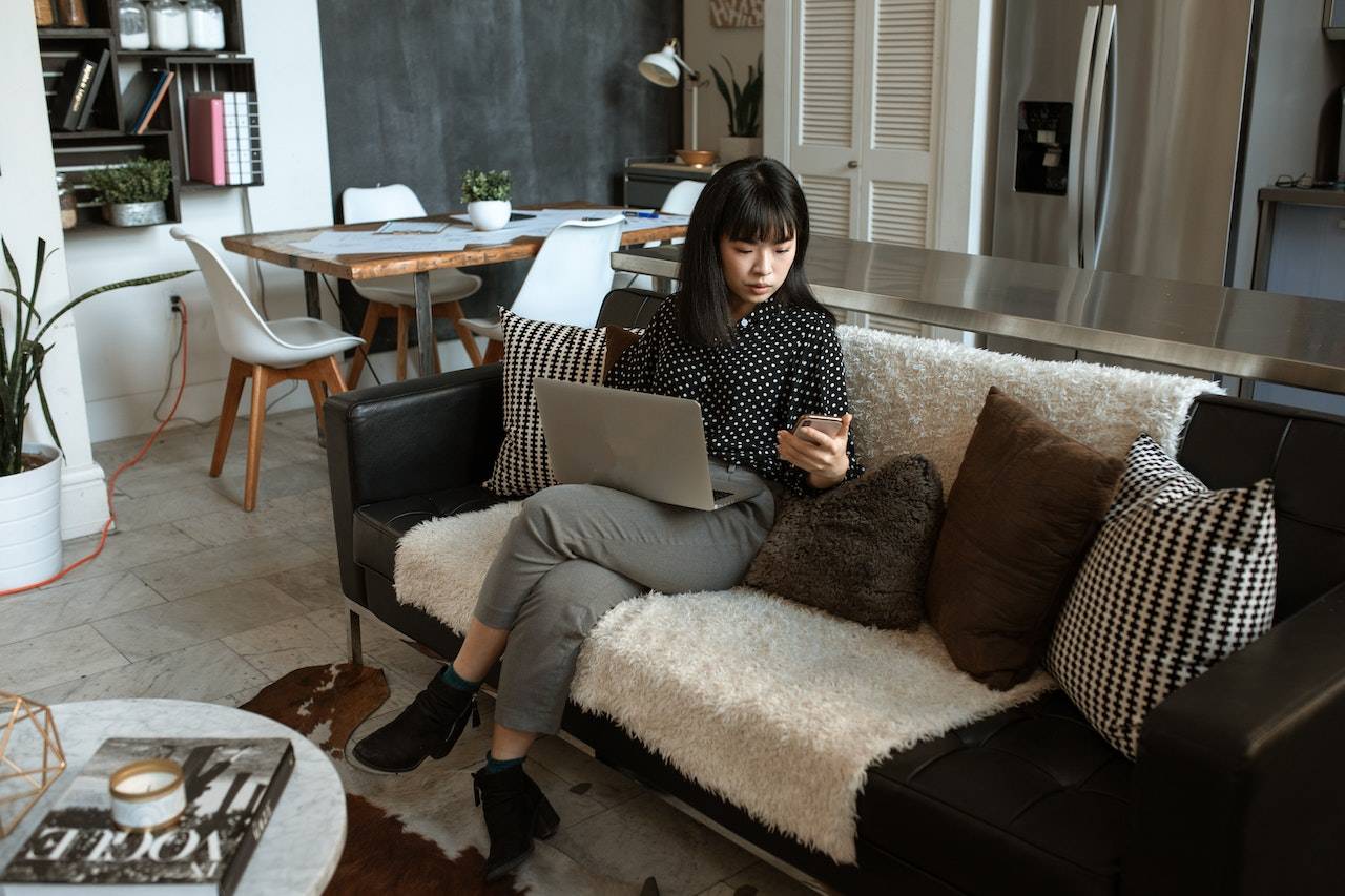 Photo of a professional checking their smartphone while working on a laptop at home.