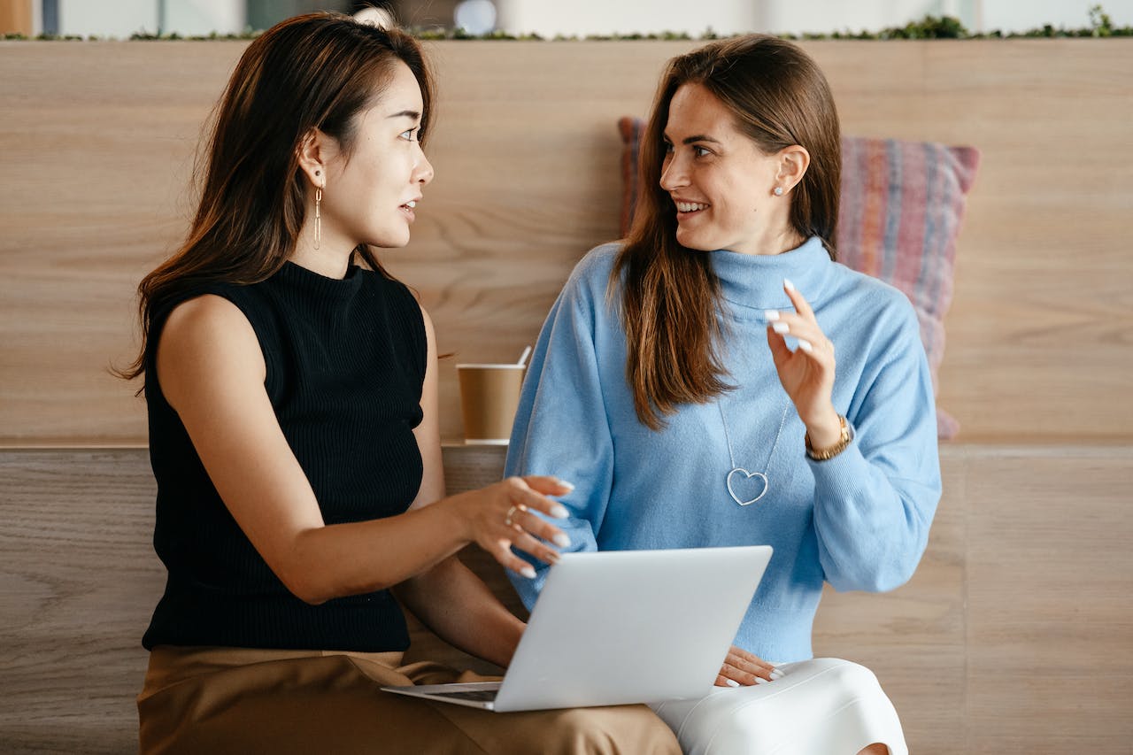 Two professionals sitting down and talking in an informal coworking space.