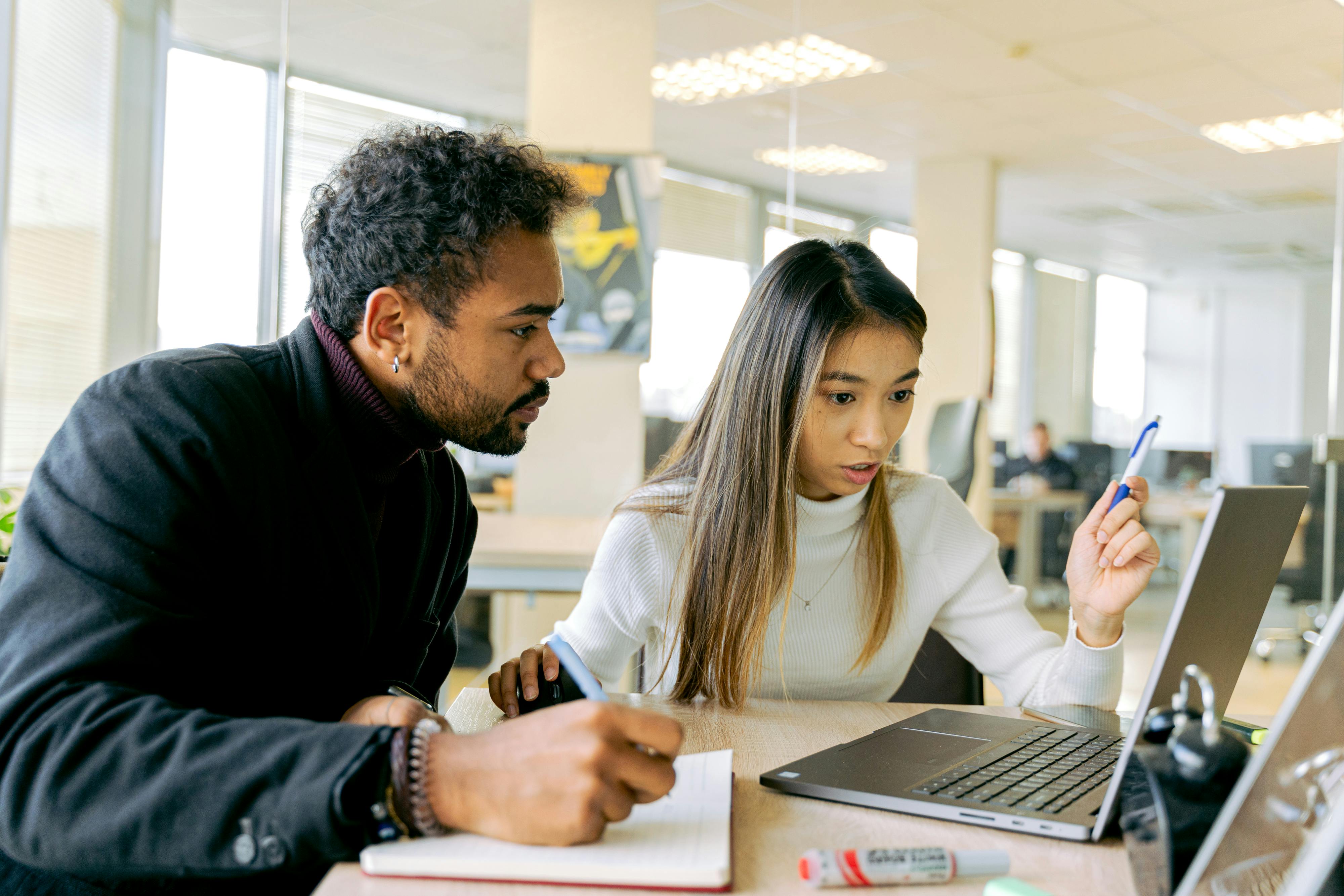 A photo of two professionals having a discussion and looking at a laptop together while sitting down.