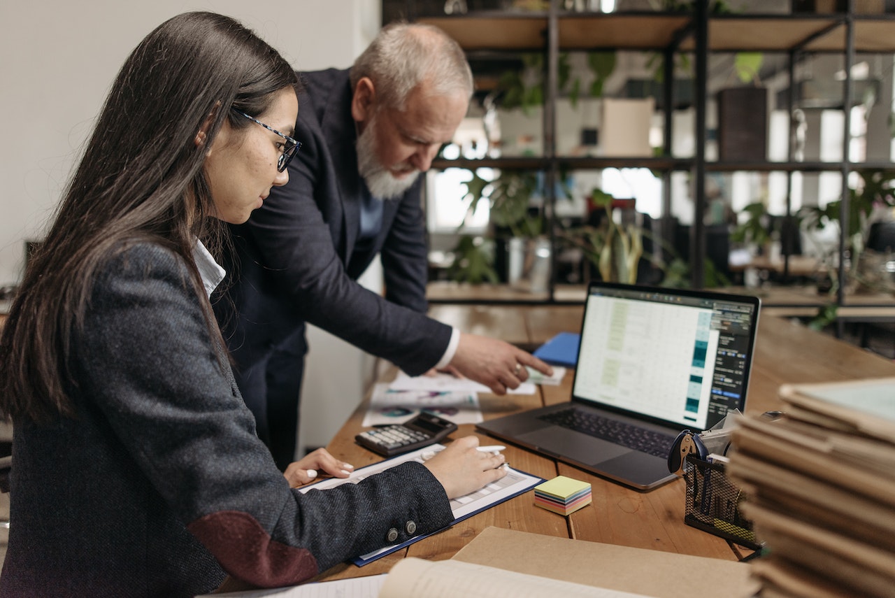 A photo of an employee pointing something out on a laptop to another employee.